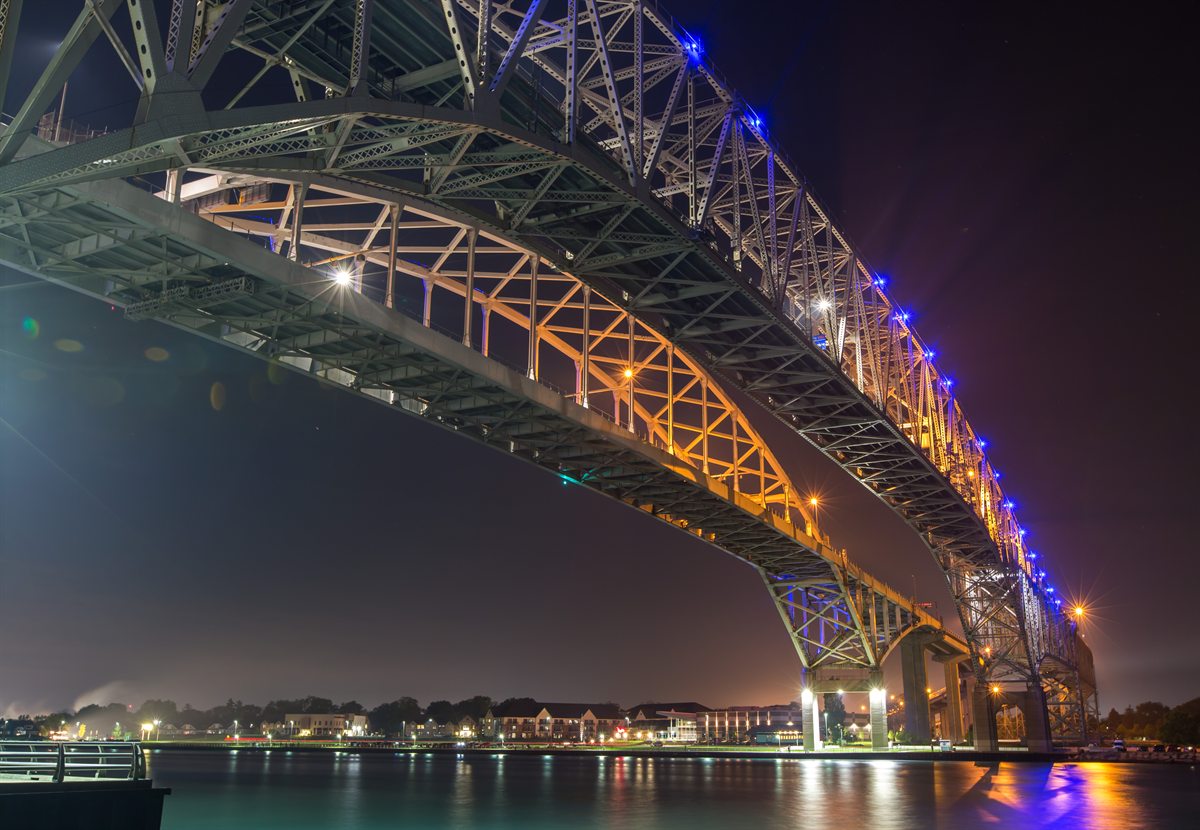 Steel bridge illuminated in blue and gold above the water at night
